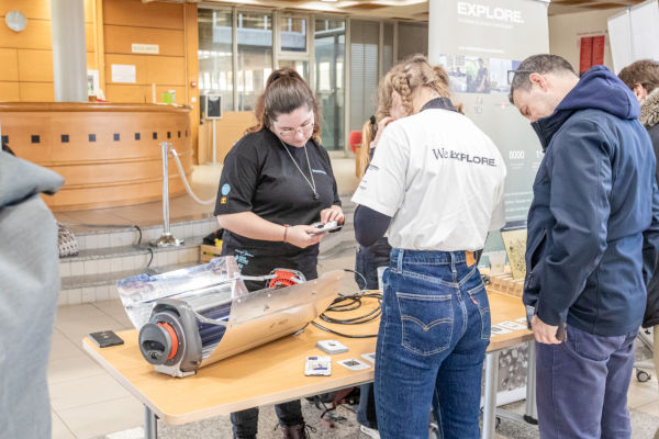 Photo du stand We Eplore : une personne montrer un objet à 2 personnes