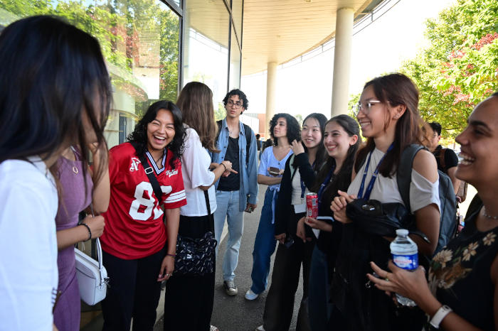 Un groupe d'une dizaine d'étudiantes et étudiants échangent sur le campus de l'école. Ces étudiantes et étudiants ont un air joyeux.