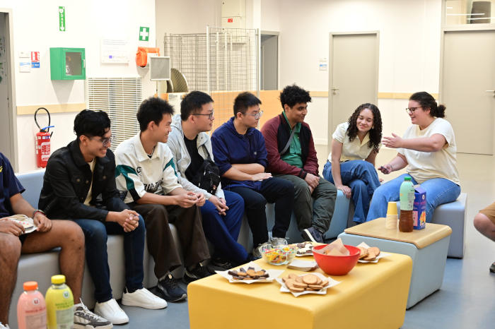 Un groupe de 6 étudiants assis sur des banquettes partagent un petit déjeuner avec une personne de la direction des relations internationales
