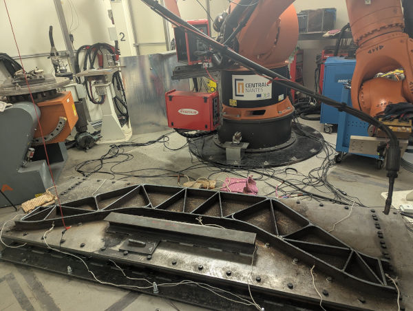 Photo. In the foreground, you can see the part that is about to be printed. In the background, you can see the machine carrying out the printing.